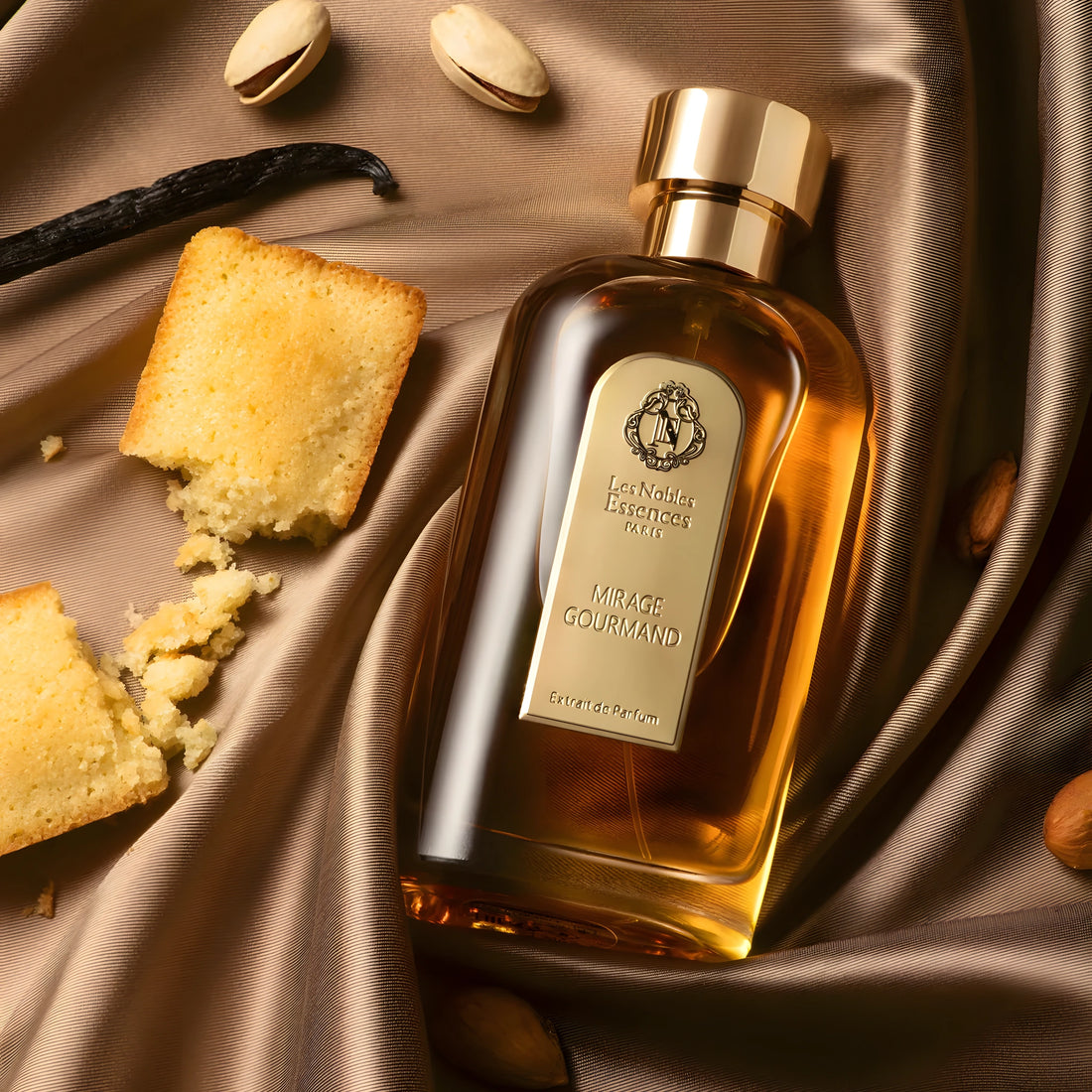 Le flacon Mirage Gourmand des Nobles Essences posé sur une soie brune, entouré de financiers, de pistaches et de gousses de vanille.