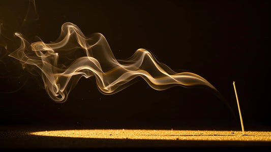 Volute de fumée dorée traversant l'obscurité au-dessus d'un sol de sable clair, image d'illustration pour un article sur le sillage d'un parfum.