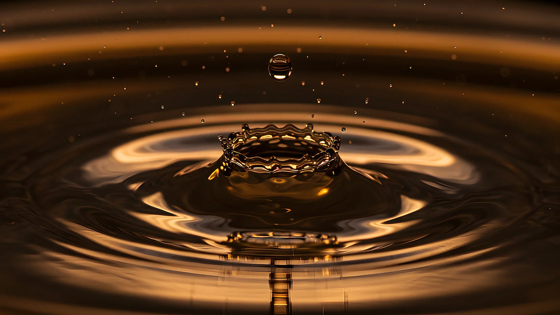 Goutte de liquide ambré frappant une surface sombre, couronne d'impact et ondes concentriques dorées, illustration des notions d'intensité, de sillage et de tenue.