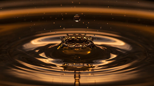 Goutte de liquide ambré frappant une surface sombre, couronne d'impact et ondes concentriques dorées, illustration des notions d'intensité, de sillage et de tenue.