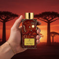 Oro Rojo AB Signature Paris — main masculine bracelet doré tenant flacon bordeaux baobabs Madagascar Antsiranana sunset