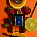 MAISON JANNOBI Soleil de Givre Extrait de Parfum 100 ml — flacon entouré d'oranges, de fraises des bois et de gousses de vanille sur fond solaire, hespéridé ambré