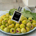 THEODOROS KALOTINIS Alluring Fig Eau de Parfum 50ml — flacon allongé sur figues vertes ouvertes et feuilles de figuier fraîches, parfumerie niche grecque ode méditerranéenne