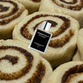 THEODOROS KALOTINIS Cinnamon Rolls Eau de Parfum 50ml — flacon allongé sur cinnamon rolls non cuits avec swirl cannelle sucre, parfumerie niche grecque gourmand pâtissier