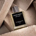 THEODOROS KALOTINIS Coffee Addict Eau de Parfum 50ml — flacon allongé sur grains de café arabica torréfiés, parfumerie niche grecque oriental gourmand